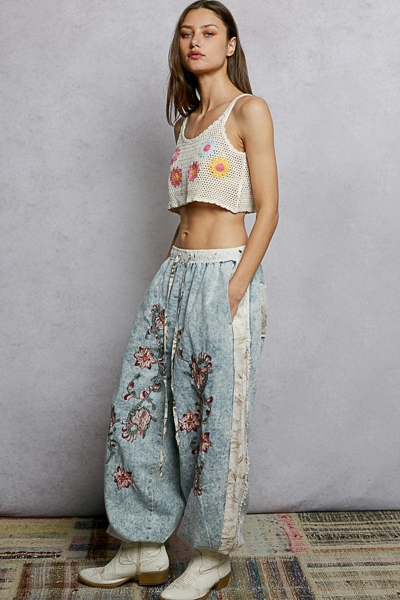 Woman wearing a floral top and wide-leg pants against a plain background