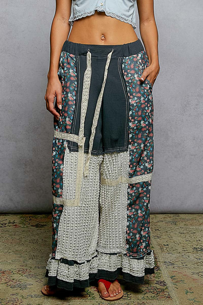 Person wearing a unique, layered outfit with floral and patterned pants against a plain background.