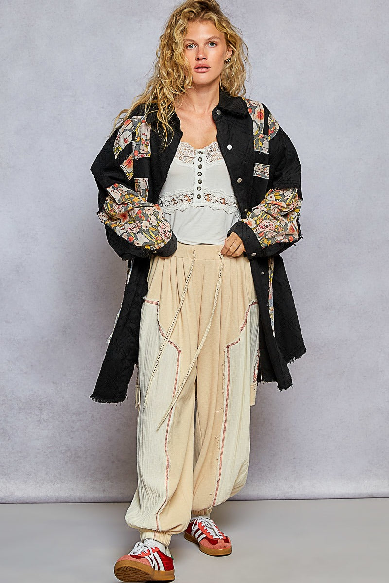 Woman wearing a stylish outfit with a floral jacket, white top, beige pants, and red shoes against a gray background.