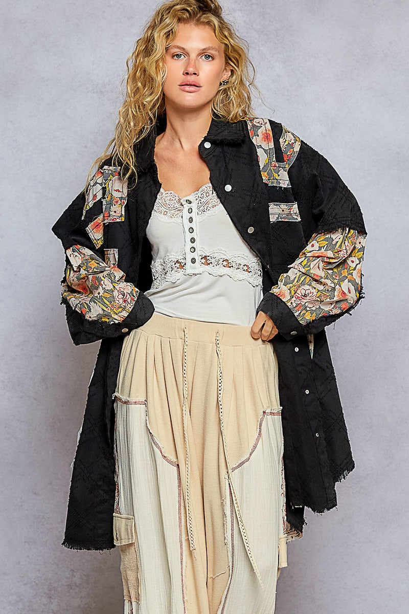 Woman wearing a black floral embroidered jacket over a white top and beige skirt on a gray background