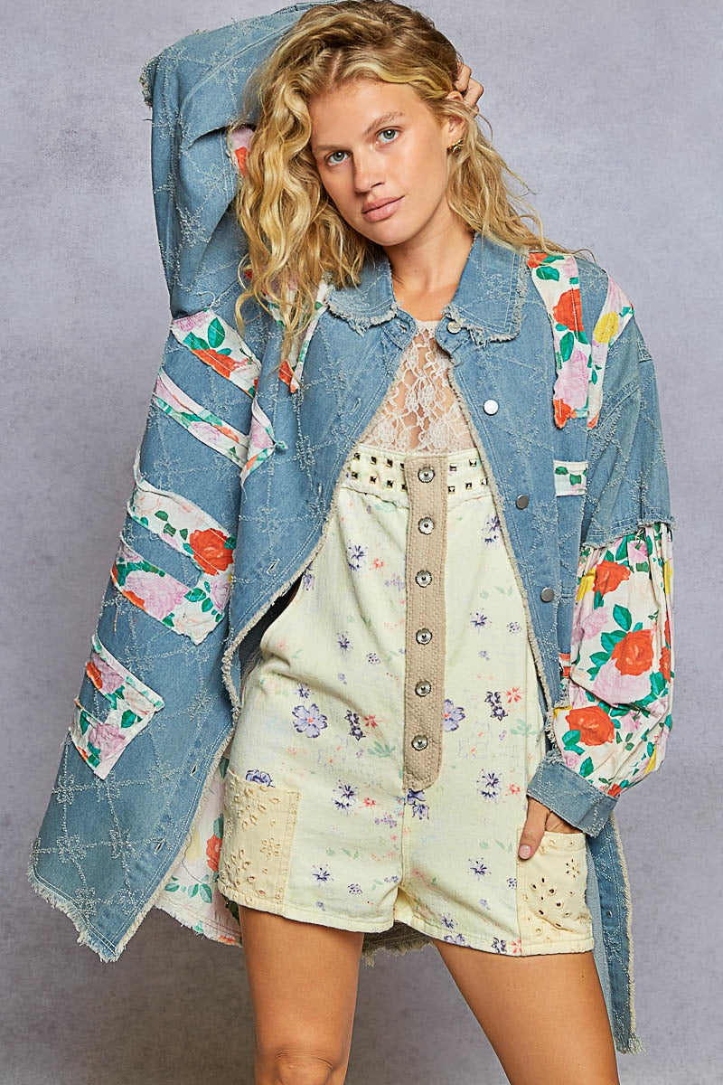 Woman wearing a floral-patterned denim jacket over a floral dress on a gray background