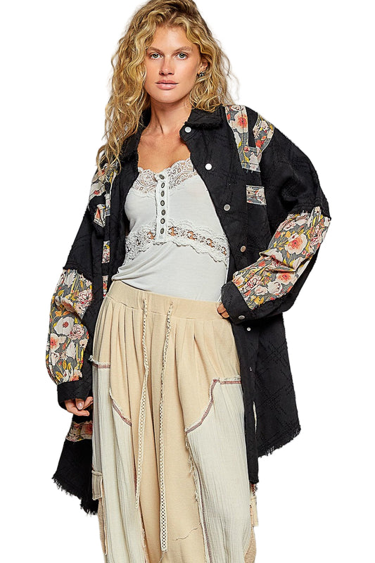 Woman wearing a black floral embroidered jacket over a light gray top and beige skirt on a white background