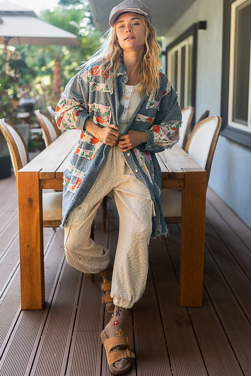 Person wearing a floral jacket and beige pants sitting on a wooden chair outdoors.