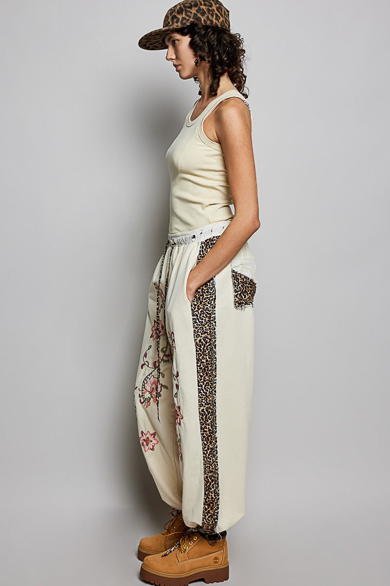 Woman wearing a cream tank top and floral pants with a leopard print cap against a gray background