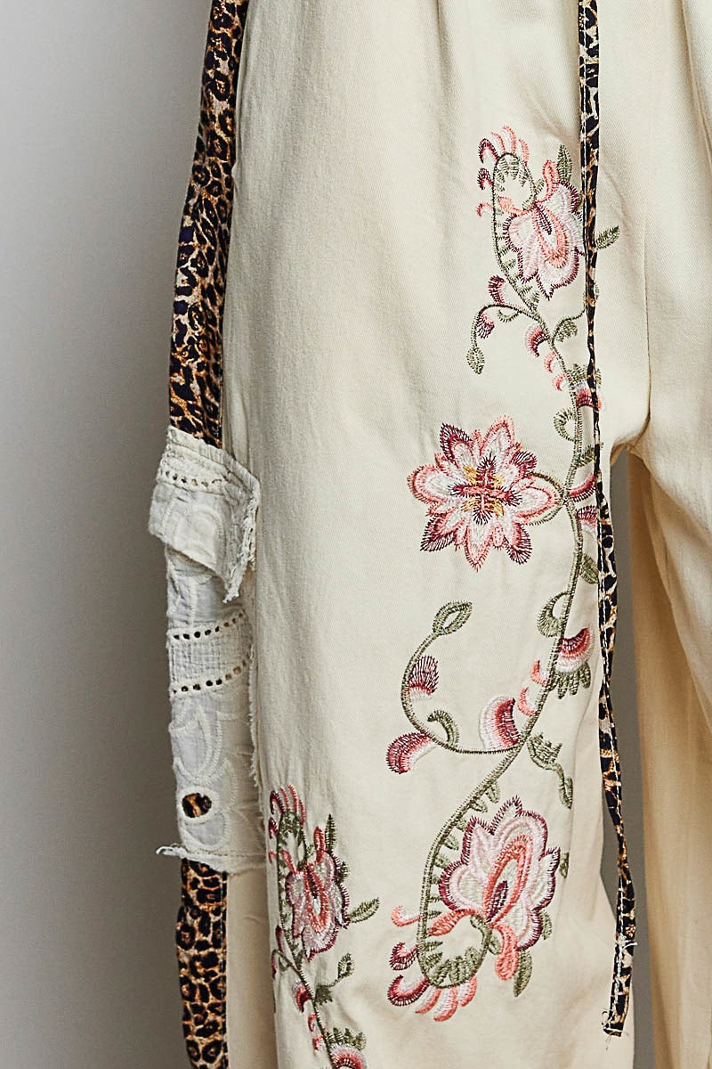 Close-up of a garment with floral embroidery and leopard print details on a neutral background