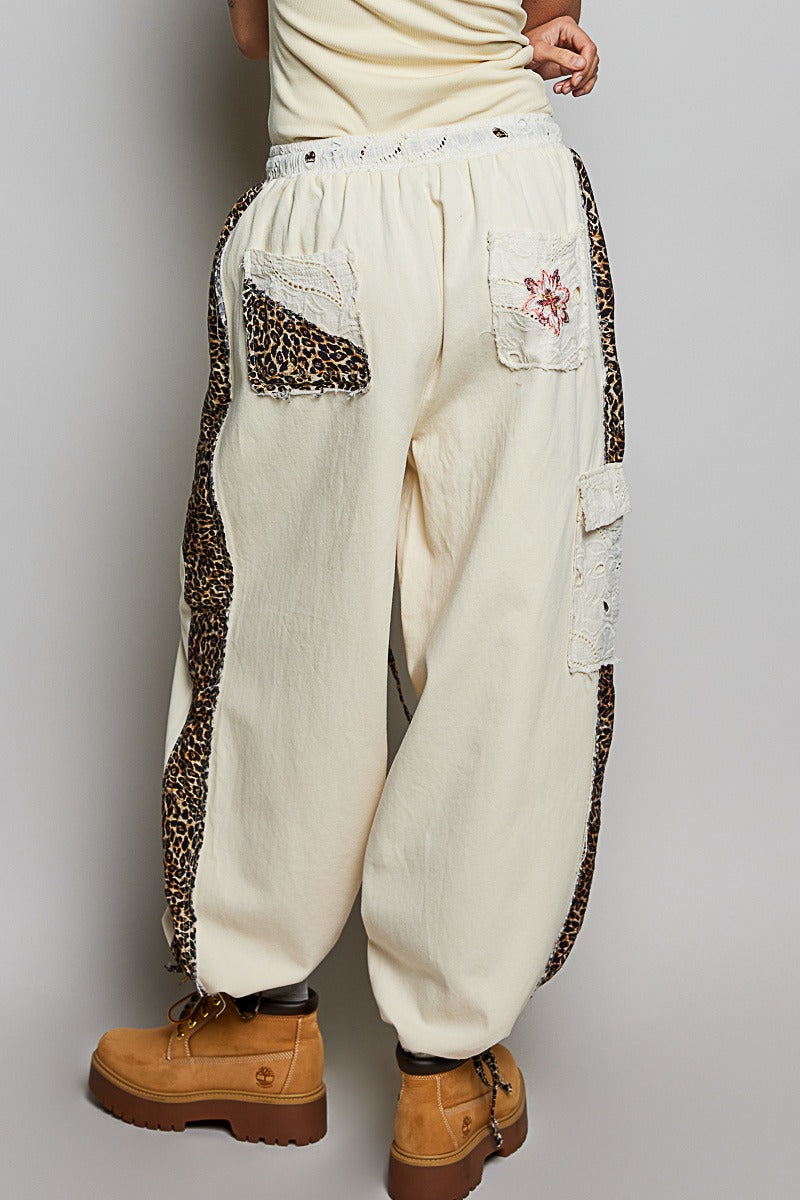 White patchwork pants with leopard print accents worn by a person on a gray background