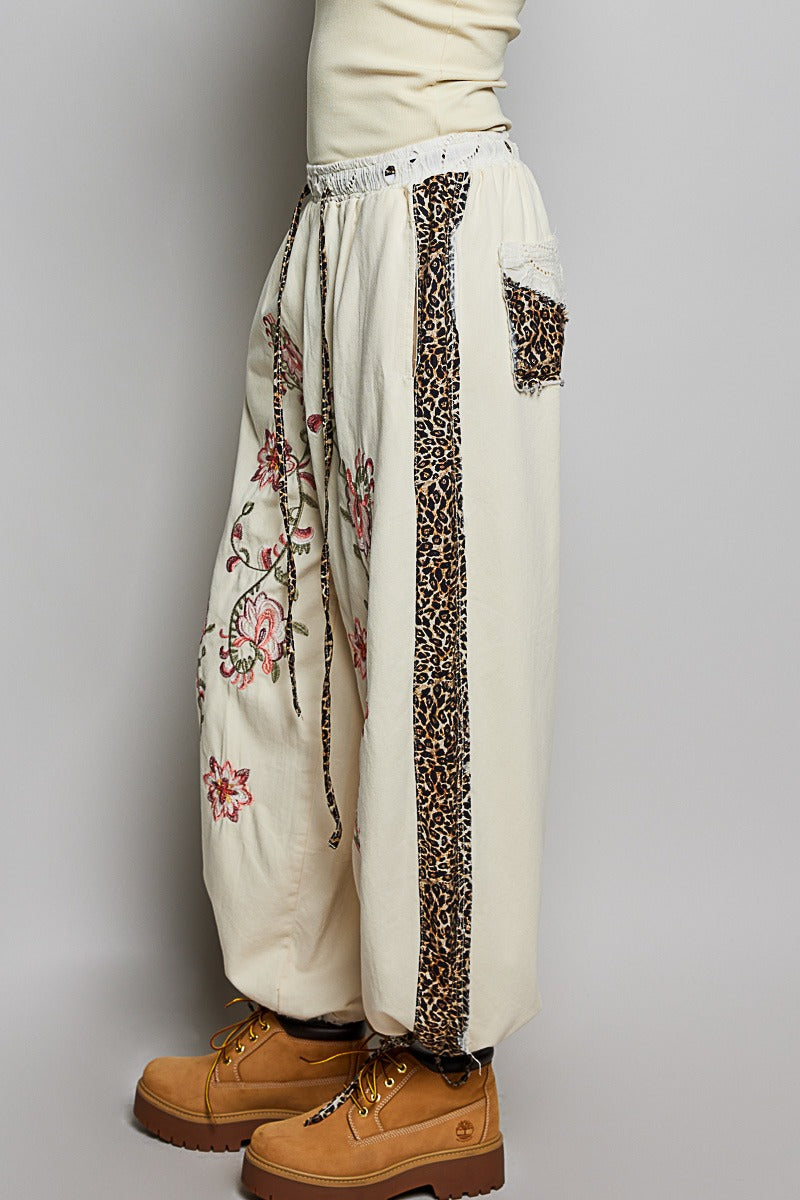 White pants with floral and leopard print accents worn by a person on a gray background