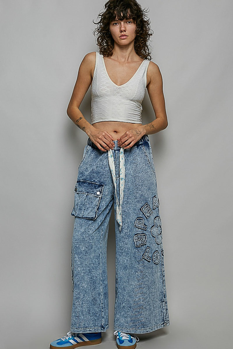 Woman wearing a white tank top and blue acid-wash jeans against a gray background