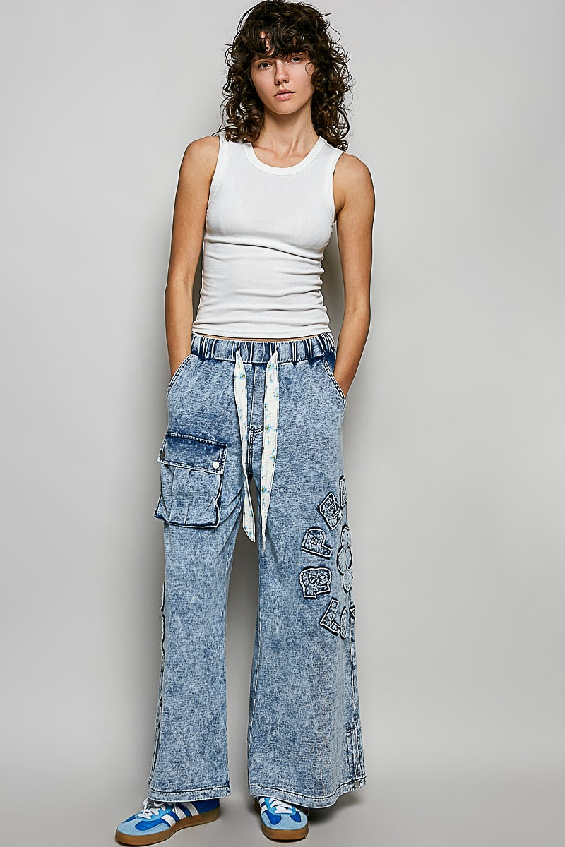 Woman wearing a white tank top and blue acid-wash cargo pants on a plain background