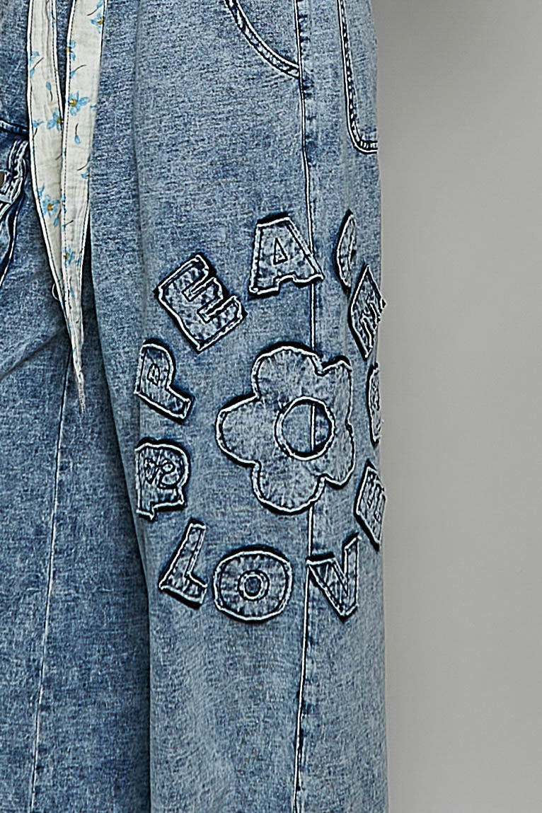 Blue jeans with floral and text embroidery on a gray background