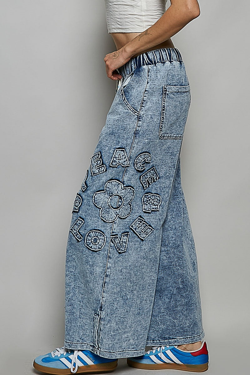 Person wearing blue acid-wash jeans with decorative patches on a plain background