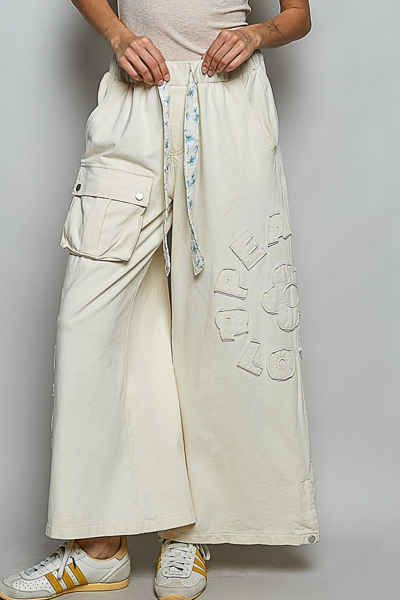 Person wearing beige wide-leg pants with text design, white sneakers, on a plain background