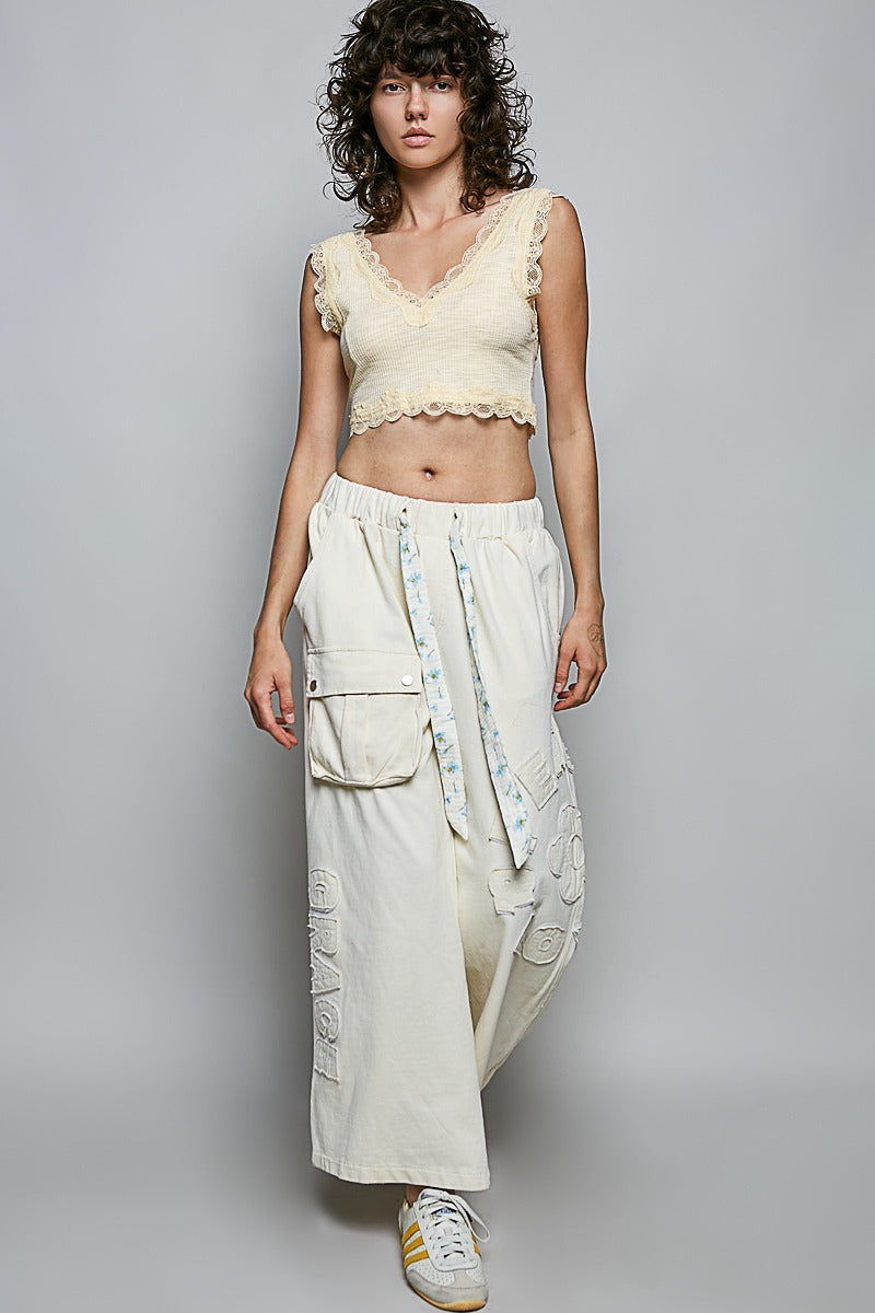 Woman wearing a light-colored top and white pants with a textured pattern against a plain background