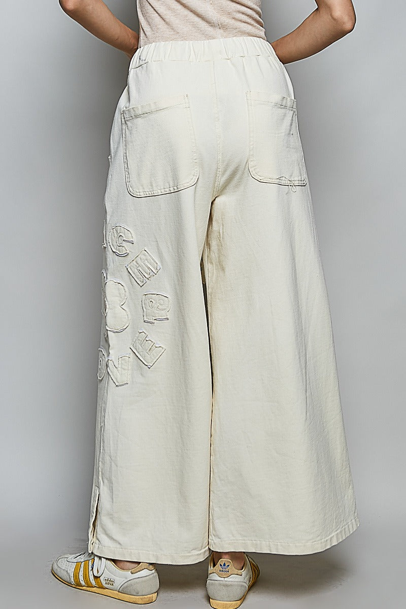 Person wearing light-colored wide-leg pants with text patterns on a plain background