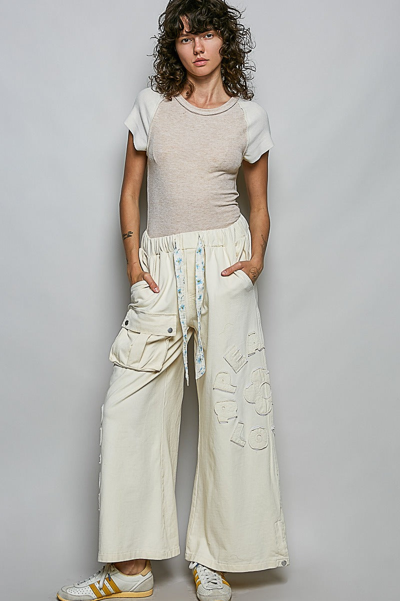 Person wearing a beige t-shirt and white wide-leg pants against a gray background