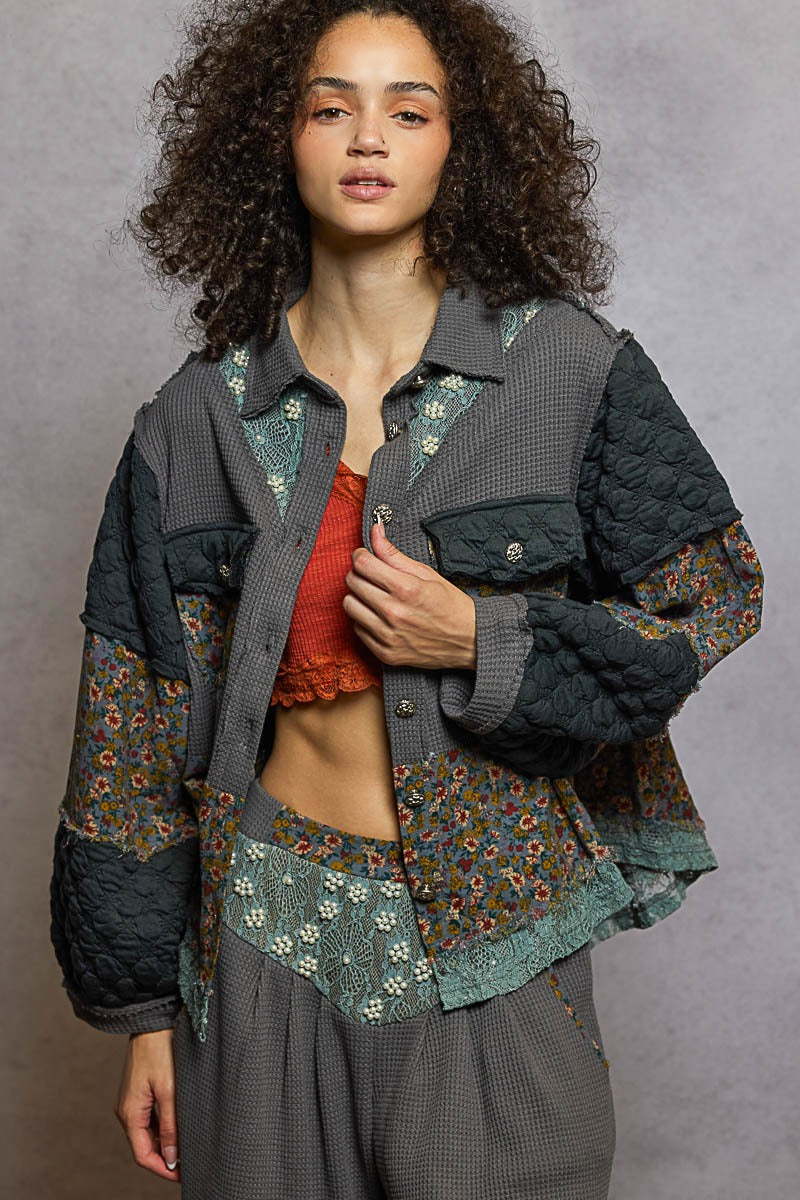 Woman wearing a layered outfit with a floral shirt and quilted jacket against a gray background