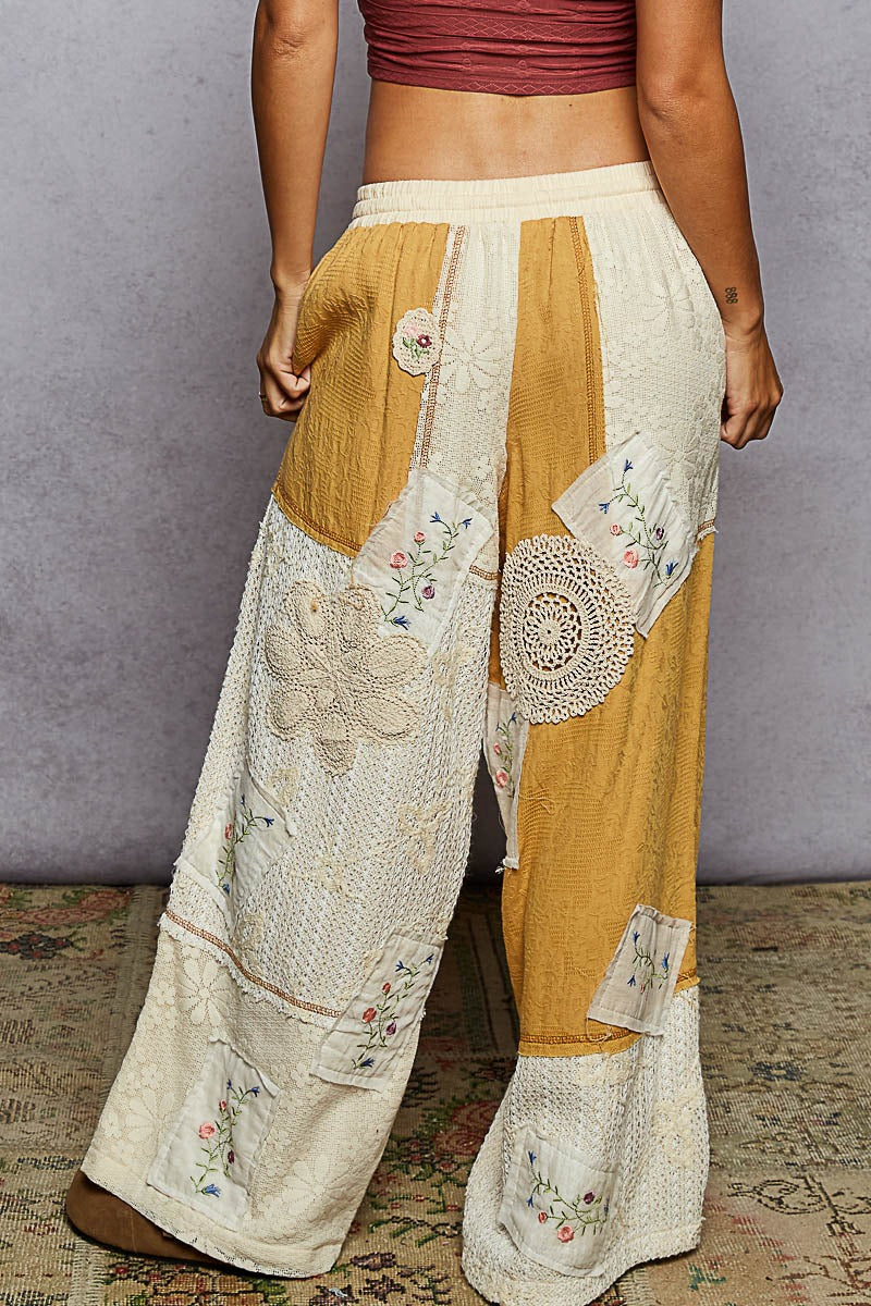 Person wearing a pair of wide-leg pants with floral and geometric patterns on a textured floor.