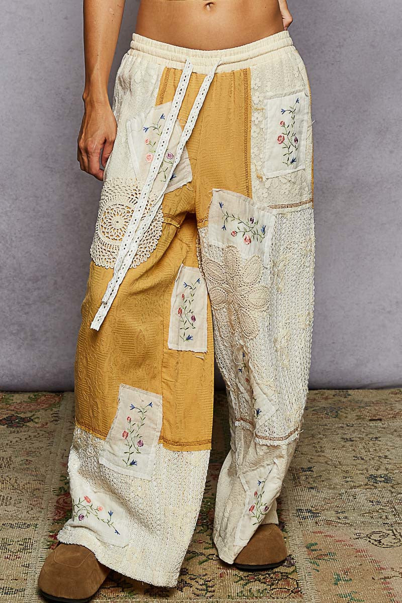 Patchwork pants with floral embroidery on a textured floor.