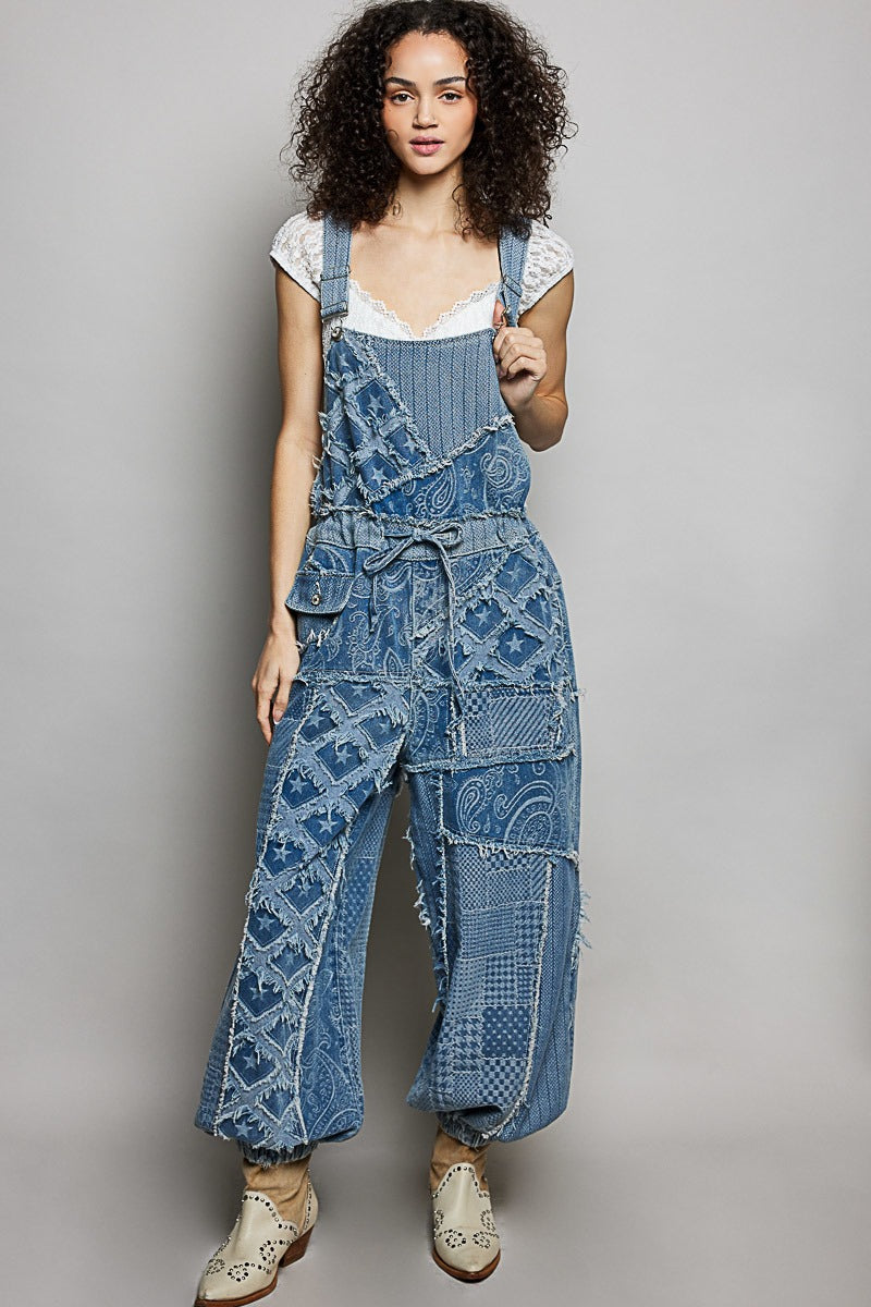 Woman wearing a blue patterned denim jumpsuit on a gray background