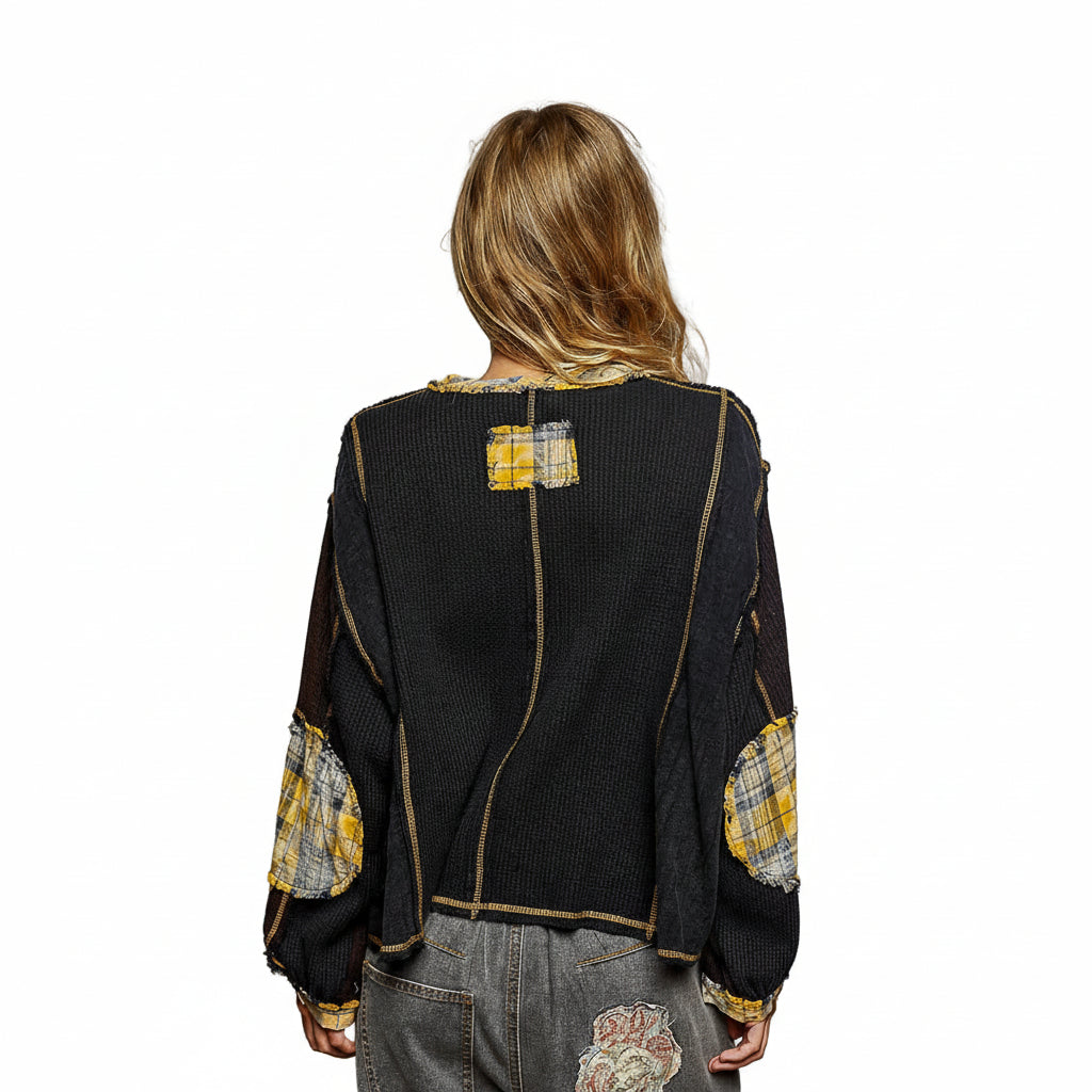 Person wearing a black jacket with yellow and white patchwork details on a gray background