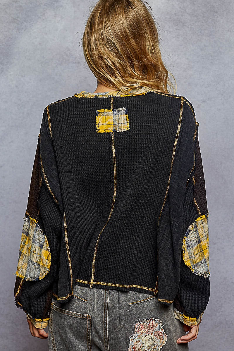 Person wearing a black jacket with yellow and white patchwork details on a gray background