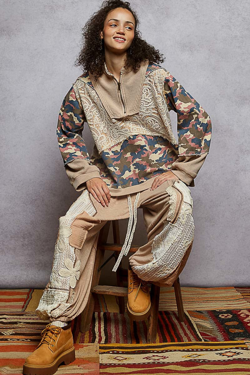 Person wearing a patchwork outfit with camouflage and beige patterns, sitting on a stool.