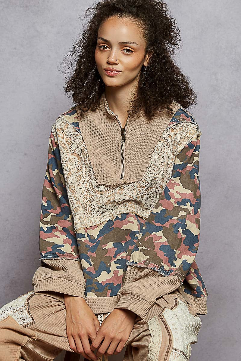 Woman wearing a camouflage and lace top against a gray background