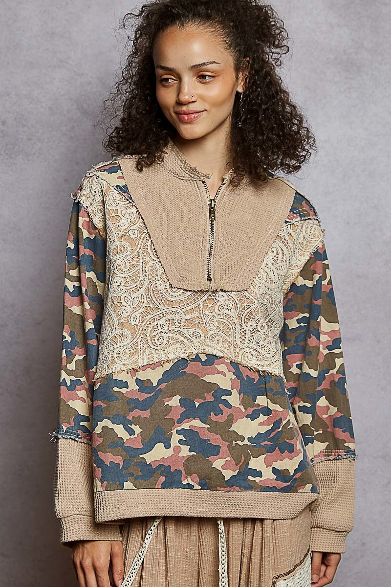 Woman wearing a unique blend of patterned and camouflage design top against a gray background