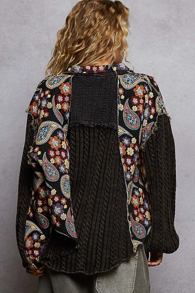 Person wearing a dark knitted cardigan with colorful paisley patterns on a gray background