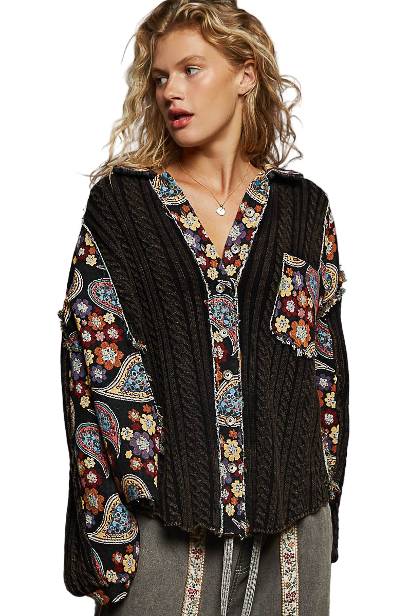 Woman wearing a black cable knit cardigan with colorful floral patterns on a gray background