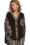 Woman wearing a black cable knit cardigan with colorful floral patterns on a gray background