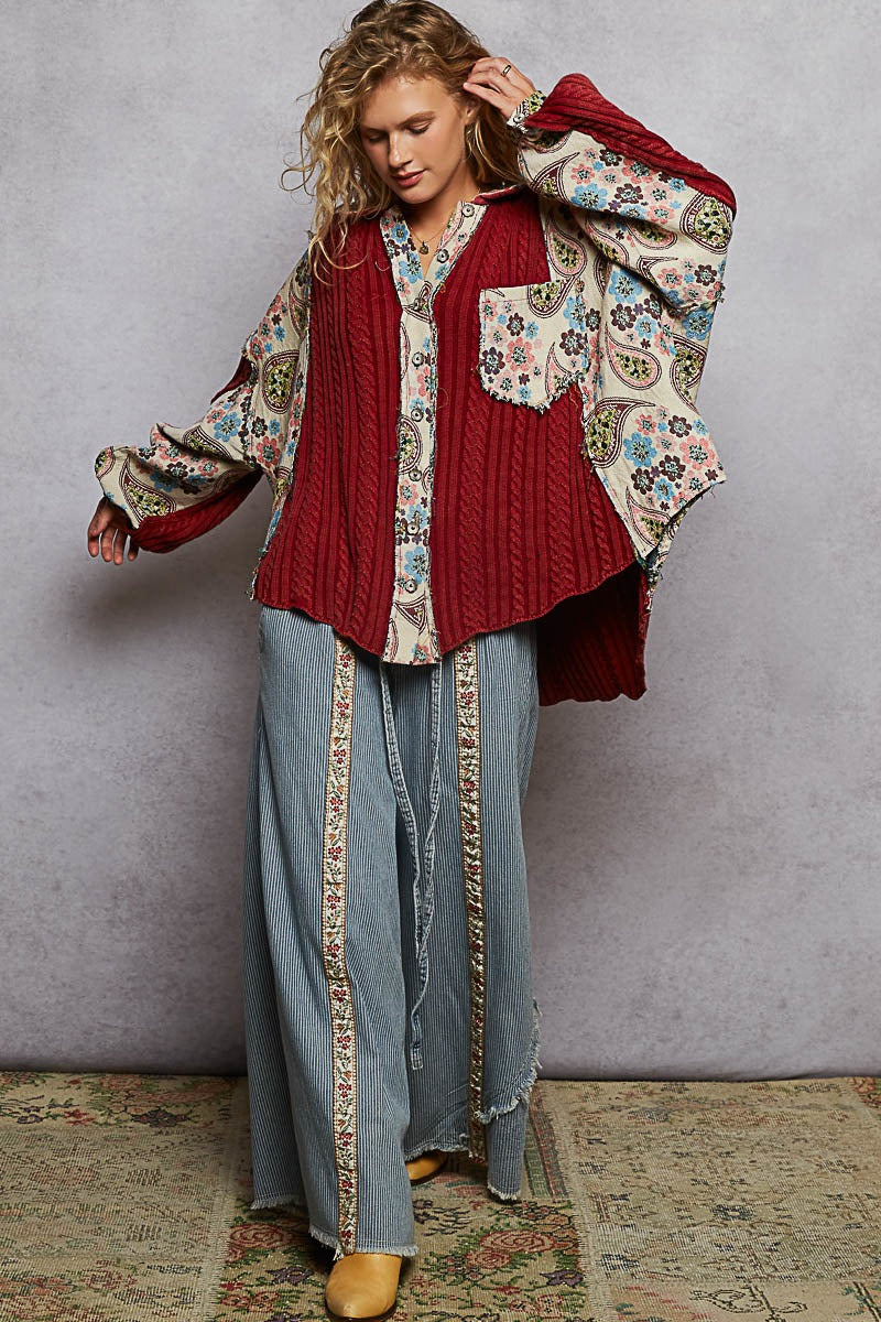 Woman wearing a floral blouse, red vest, and blue pants with a patterned rug underneath.