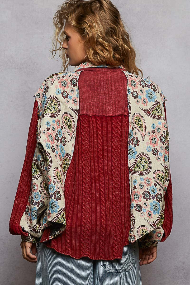 Woman wearing a red sweater with a floral patterned cardigan over it against a gray background