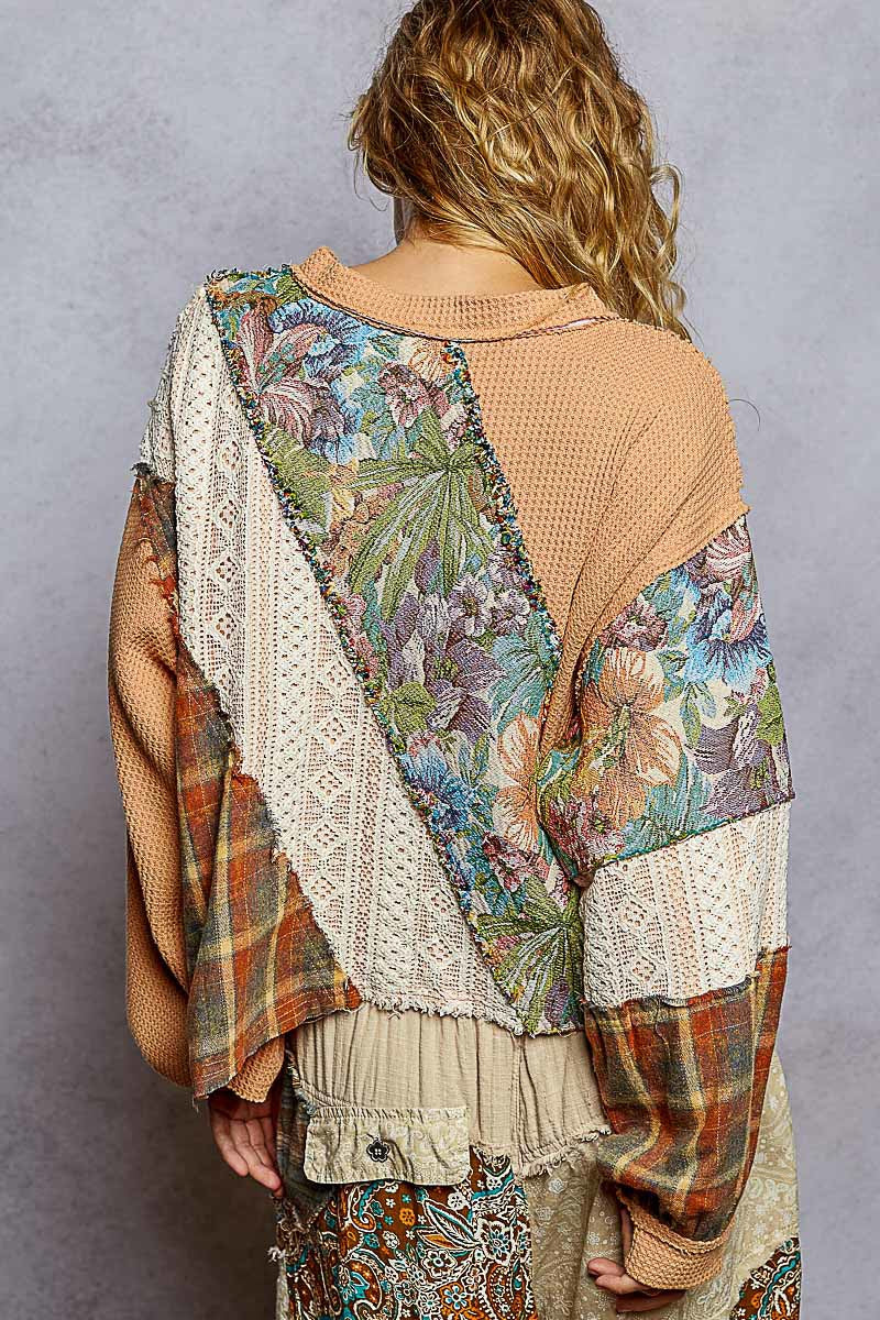 Person wearing a colorful, patterned top with a textured beige sweater over it against a gray background.