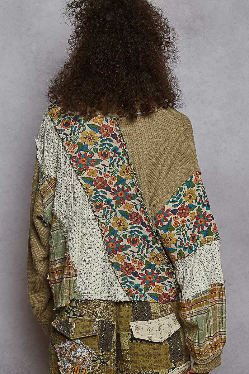 Person wearing a patchwork jacket with floral patterns on a plain background