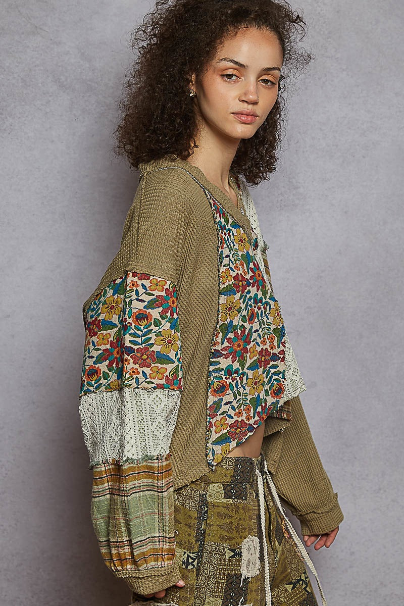 Woman wearing a patchwork cardigan over a floral blouse against a gray background