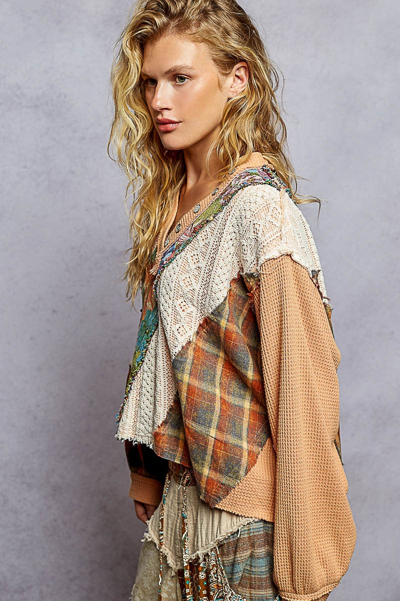 Woman wearing a layered outfit with a plaid shirt and beige cardigan against a gray background