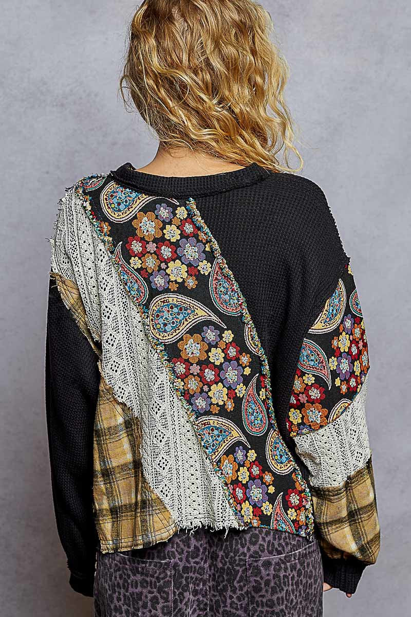 Person wearing a black sweater with colorful paisley patterns on the back, standing against a gray background.