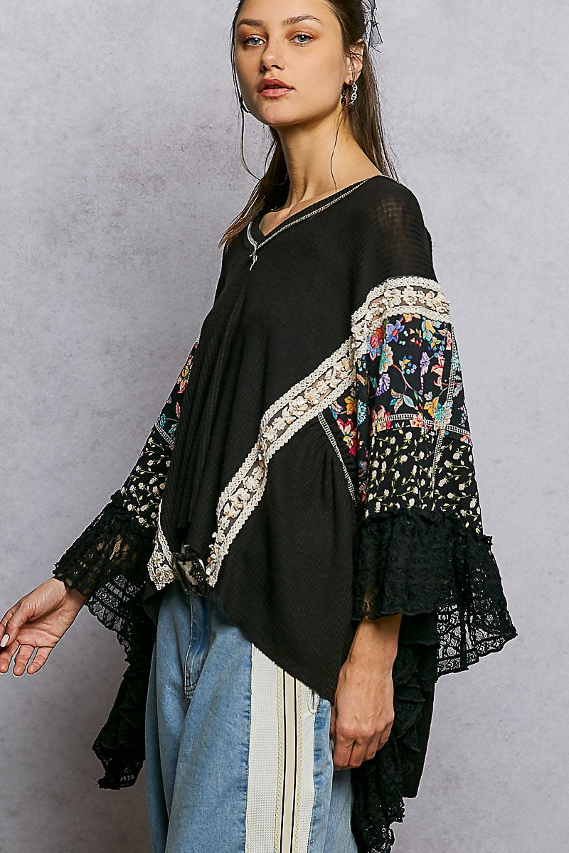 Woman wearing a black top with floral embroidery and ruffled sleeves against a gray background