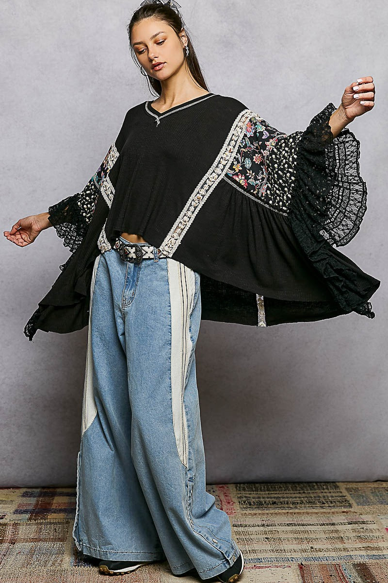 Woman wearing a black top with floral embroidery and blue jeans against a gray background