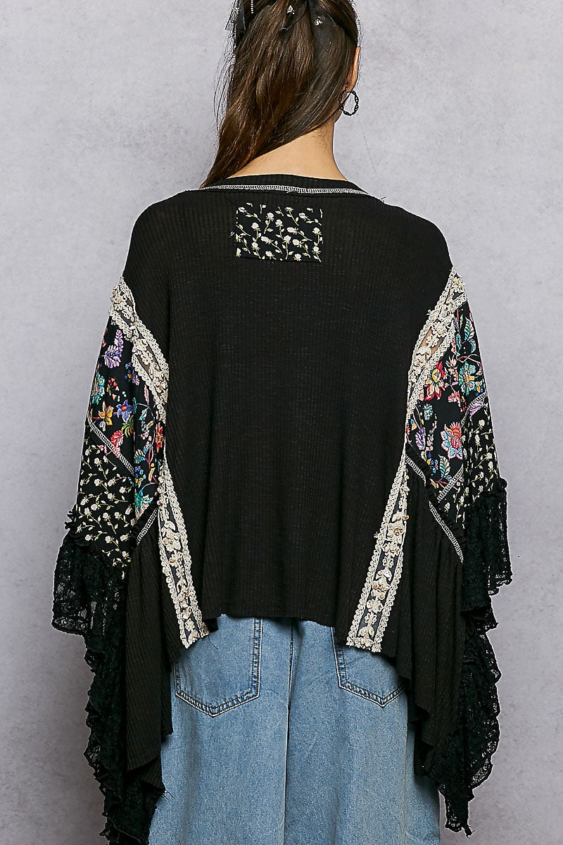 Person wearing a black top with floral embroidery and light blue jeans on a gray background