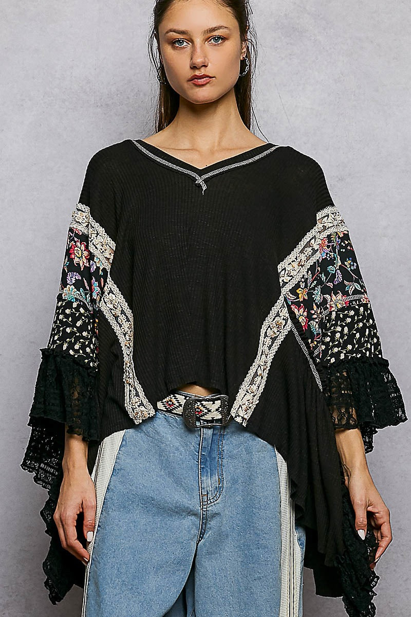 Woman wearing a black top with floral embroidery and blue jeans on a gray background