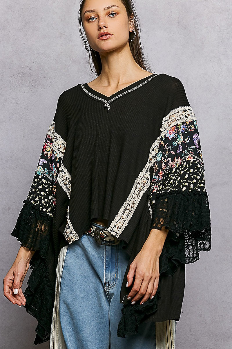 Woman wearing a black top with floral embroidery and blue jeans against a gray background