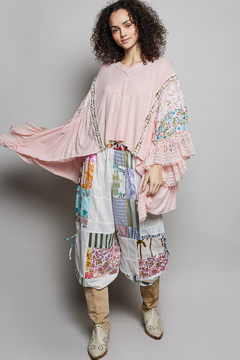 Woman wearing a pink floral top and colorful patchwork pants on a gray background