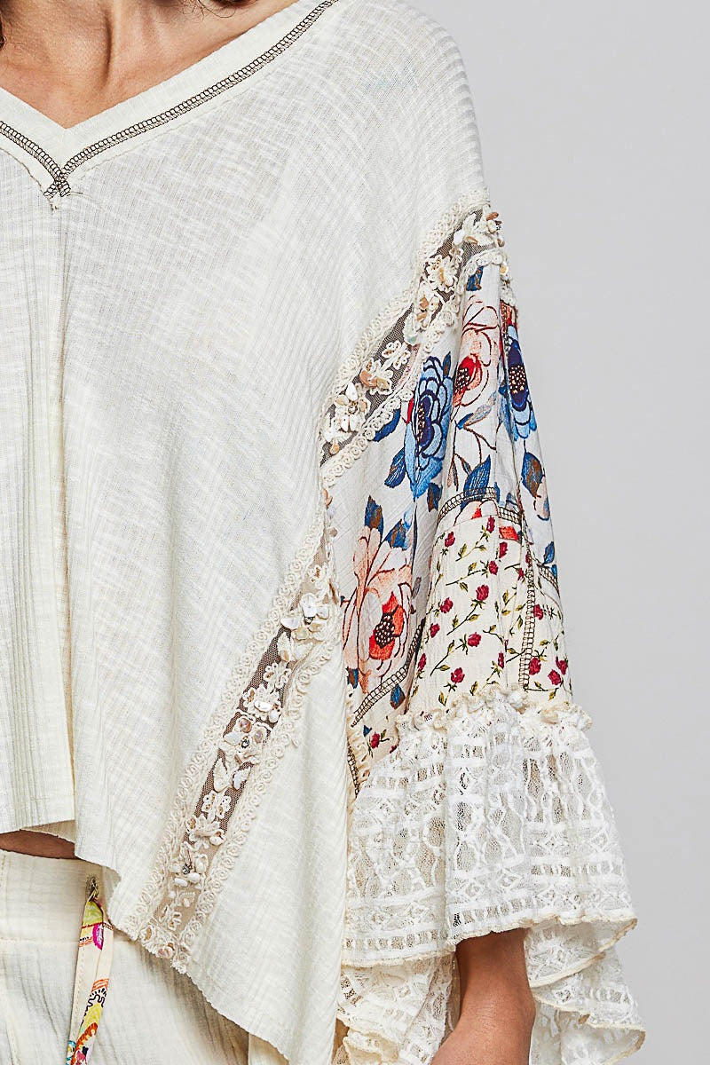 White blouse with floral embroidery on sleeves against a light gray background