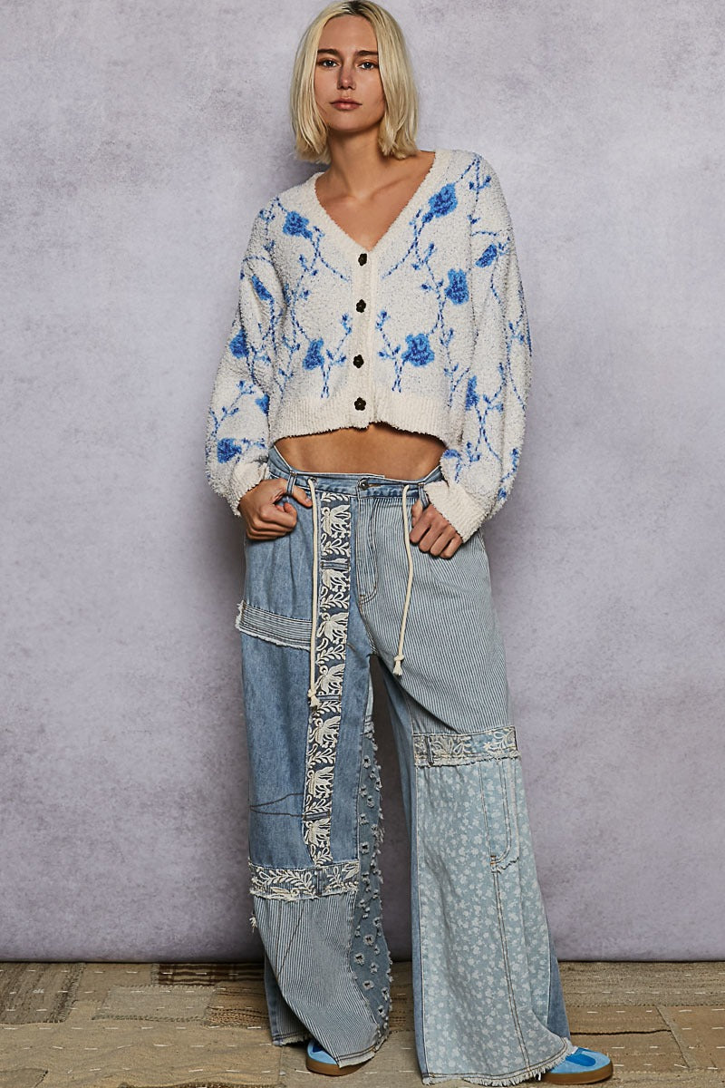 Person wearing a floral cardigan and wide-leg jeans against a plain background