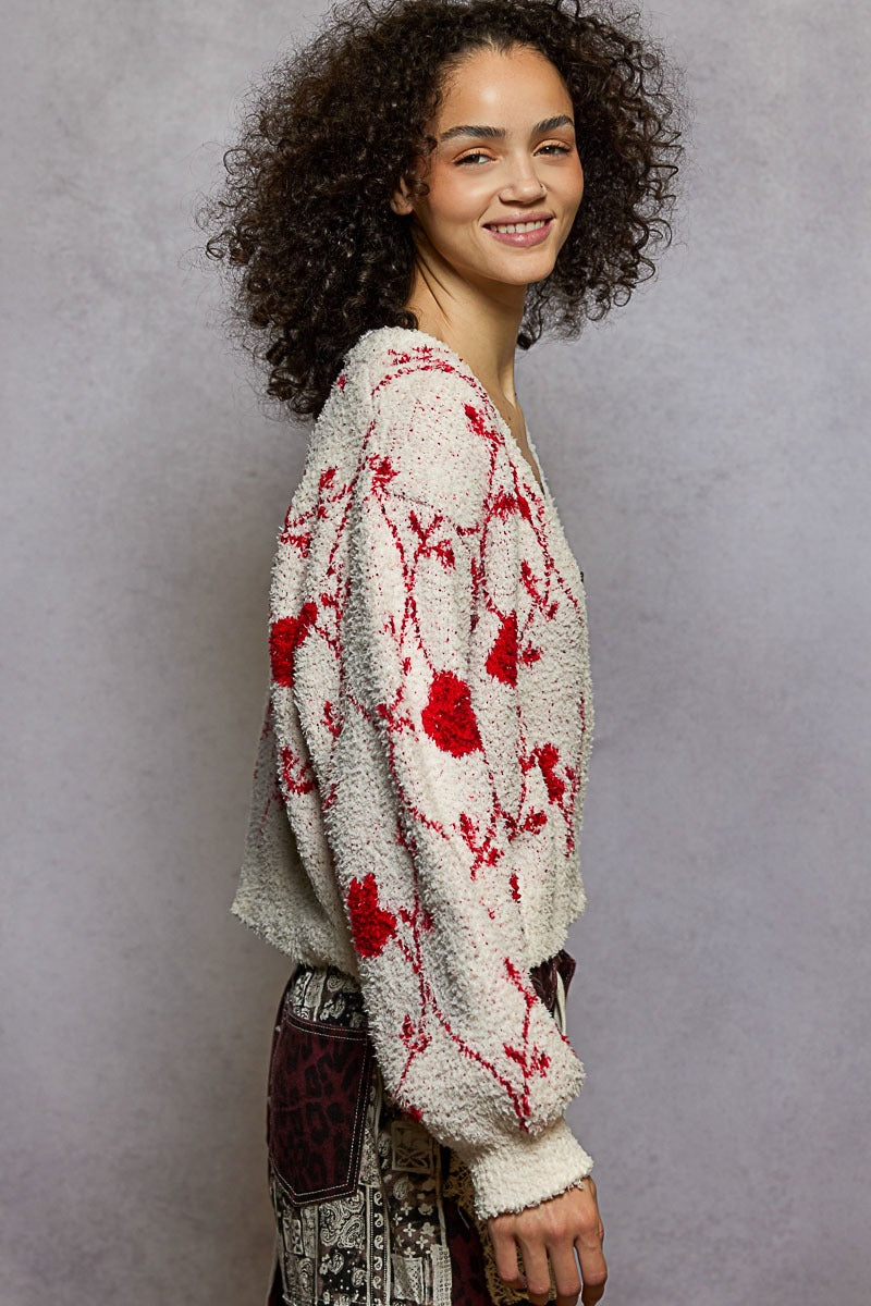 Woman wearing a cream sweater with red floral patterns against a gray background