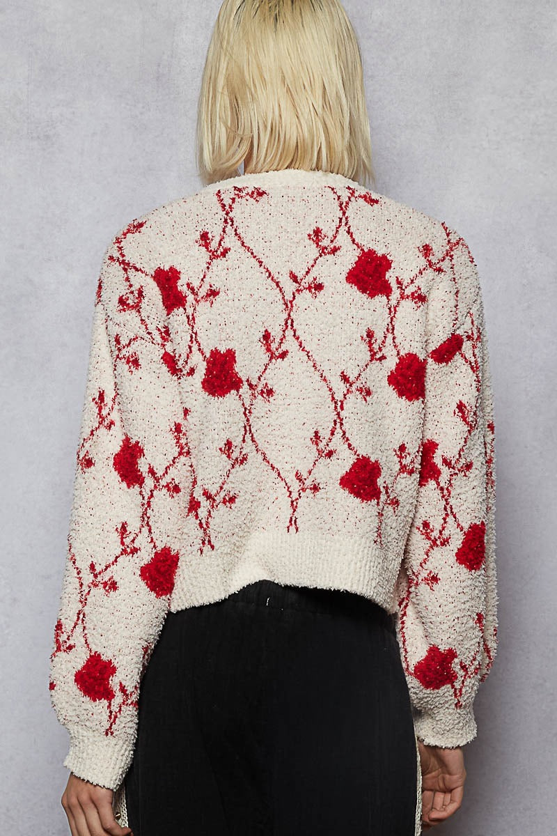 Person wearing a cream cardigan with red floral patterns against a gray background