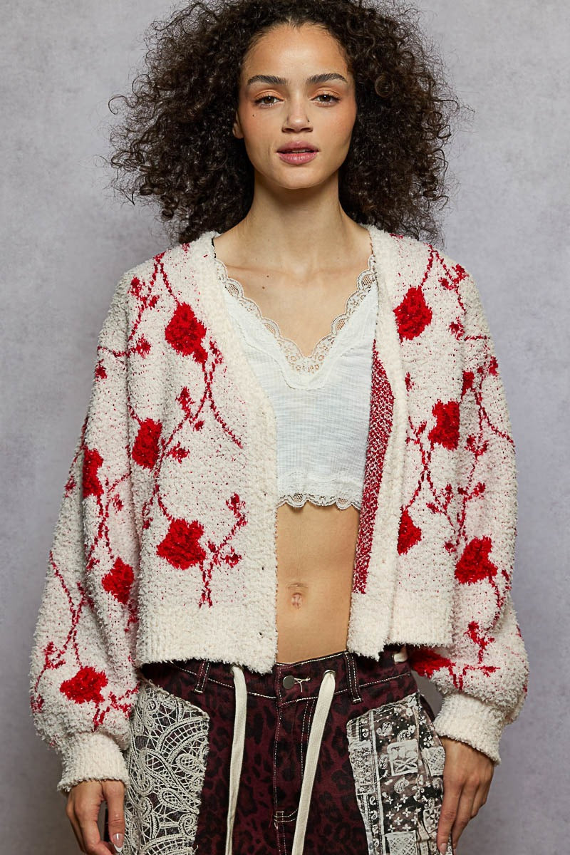 Woman wearing a white cardigan with red floral patterns on a gray background