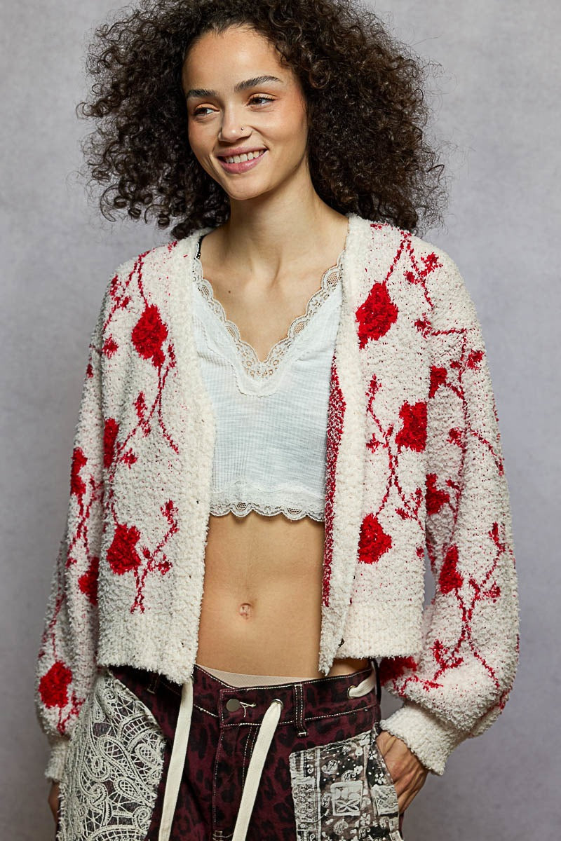 Woman wearing a white cardigan with red floral patterns on a gray background